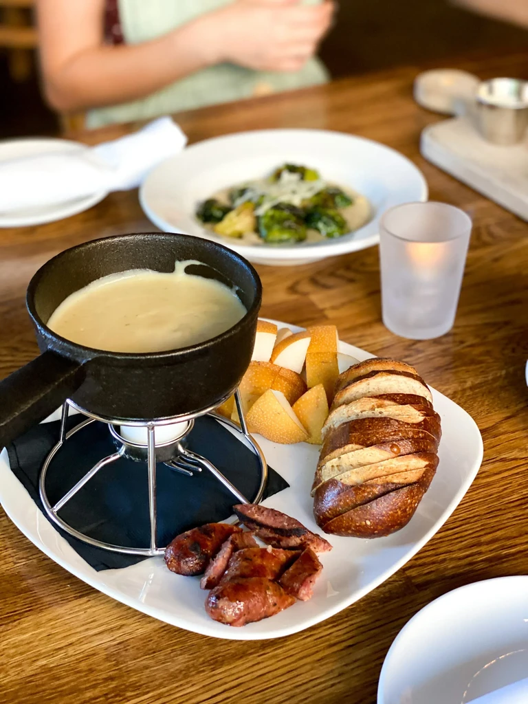 Black cast-iron fondue pot with cheese, bread, sausage, and vegetables.