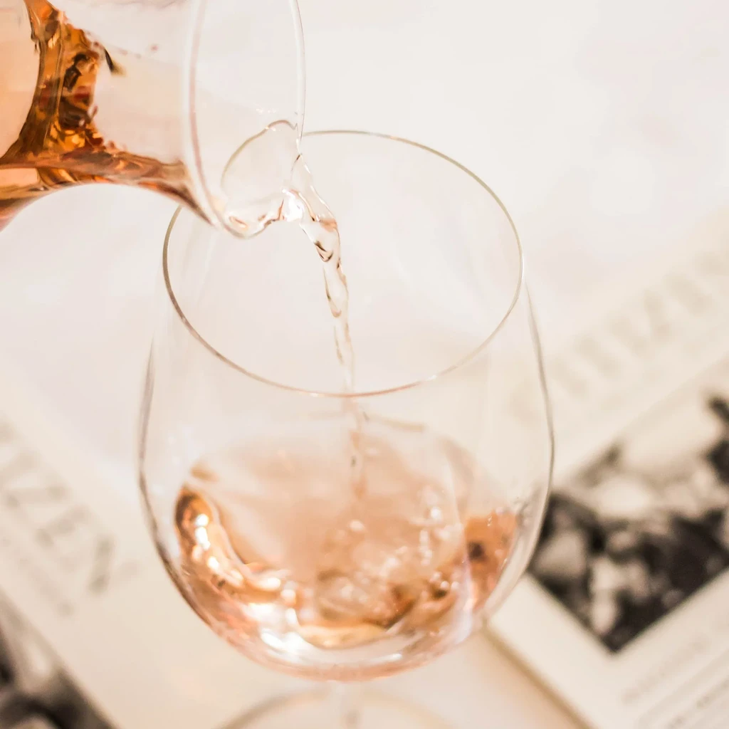 Light pink rosé wine pours from a carafe into a stemmed glass.