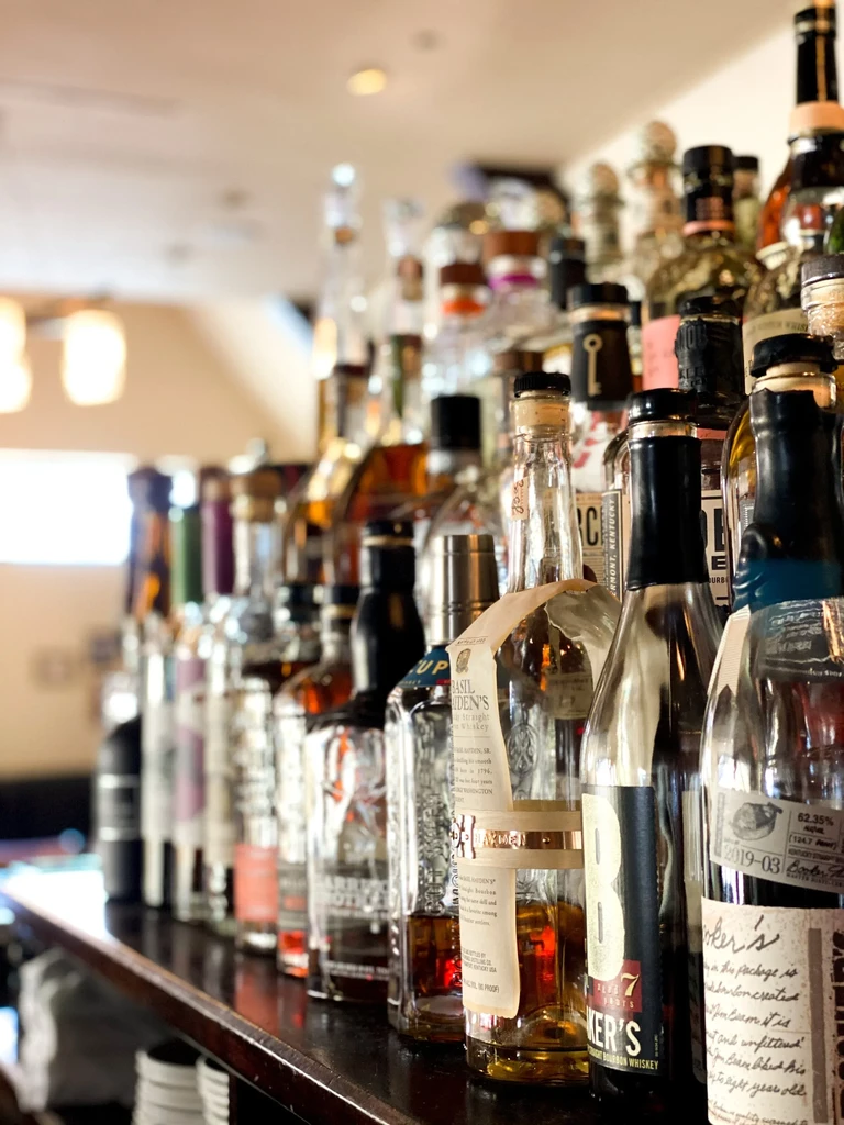 Numerous whiskey and bourbon bottles sharply focused on a dark bar shelf.