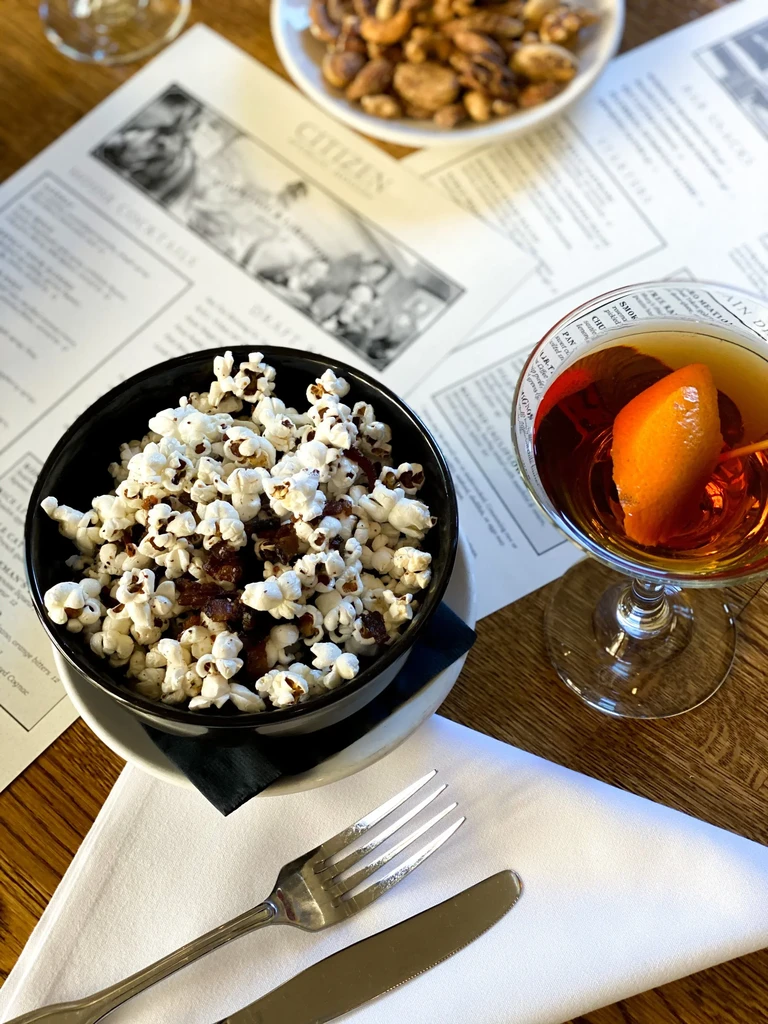 A restaurant table set with popcorn, cocktail, silverware, and menus.
