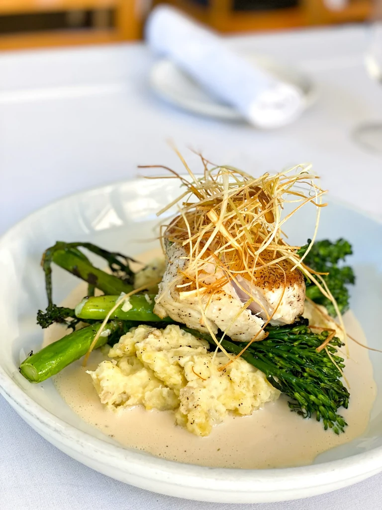 Pan-seared fish with crispy leeks, mashed potatoes, and green vegetables.