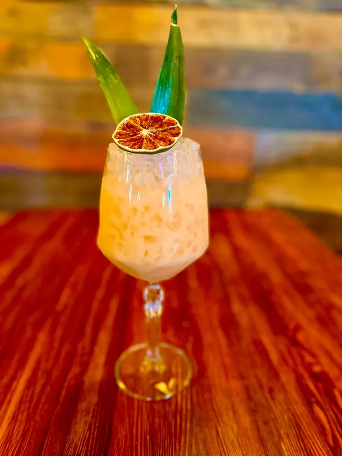 Creamy cocktail with green leaves and dried orange slice on wood.