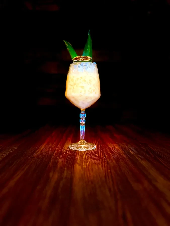Creamy cocktail in ornate glass with leaves and caramelized citrus.