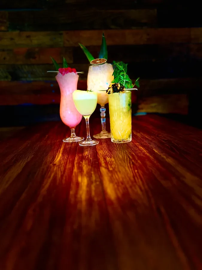 Four colorful, elaborately garnished cocktails on a dark table.