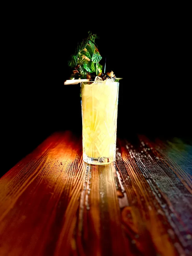 Yellow cocktail with crushed ice and mint on a polished wooden surface.