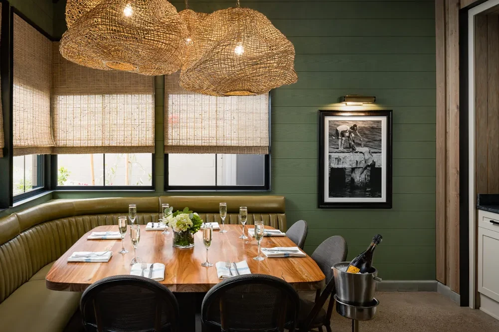 Upscale restaurant dining area with live-edge table, green banquette, and pendant lights.