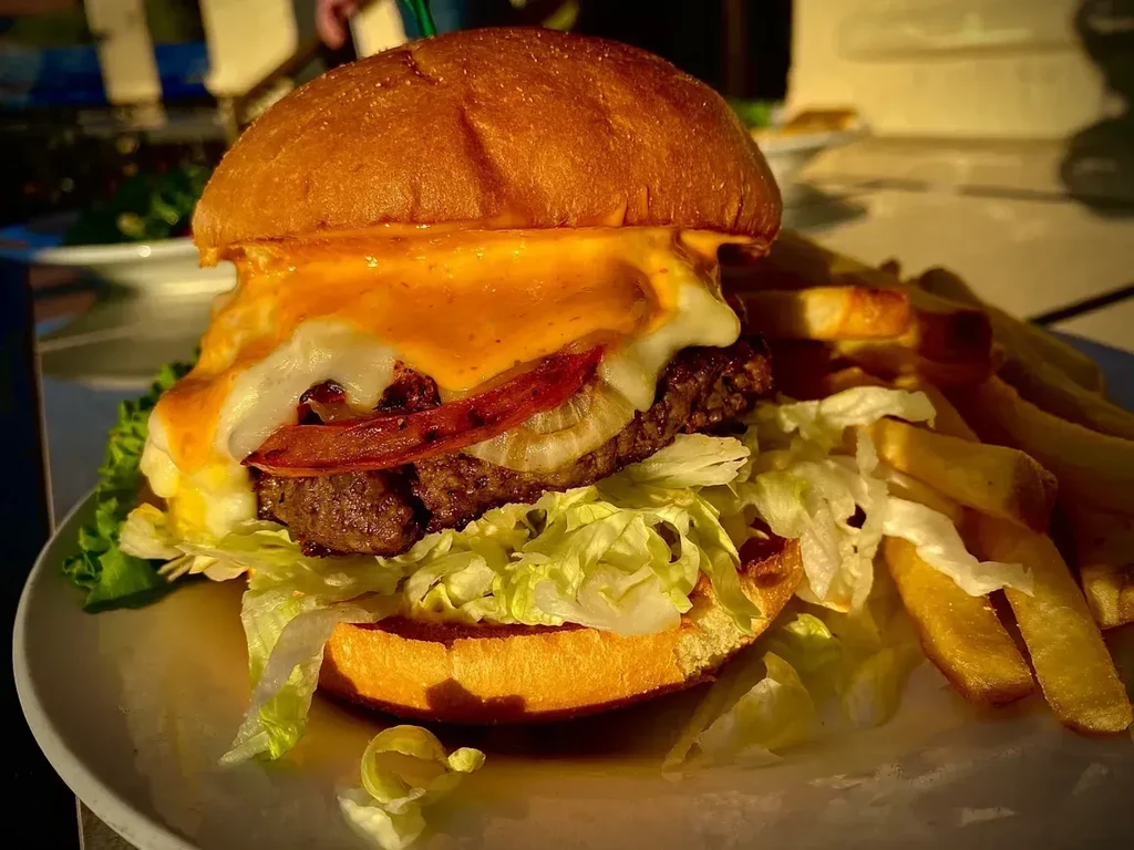 Large burger with melted cheese, various toppings, and french fries.
