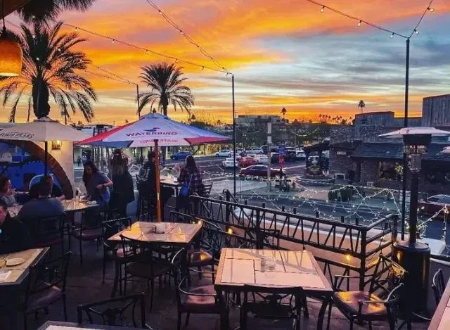 Vibrant restaurant patio at sunset with colorful sky and patrons.