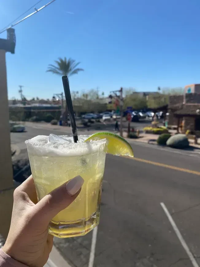 A hand holds a salted margarita with lime overlooking a sunny street.