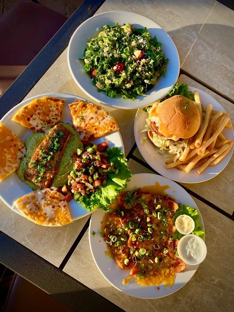 High-angle photo of four diverse meals on a sunlit outdoor table.
