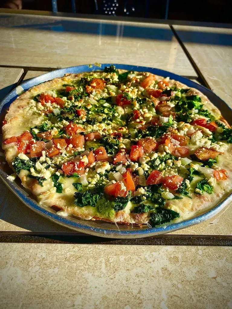 Round pizza topped with spinach, tomatoes, feta, and onions.