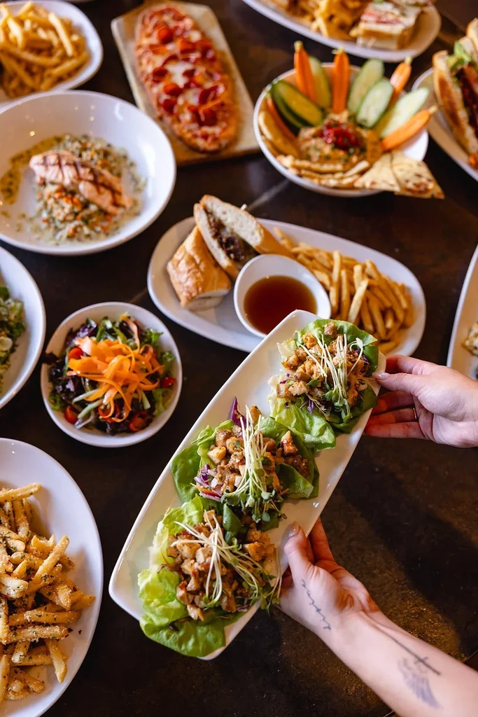 Overhead view of a diverse restaurant meal spread on a dark table.
