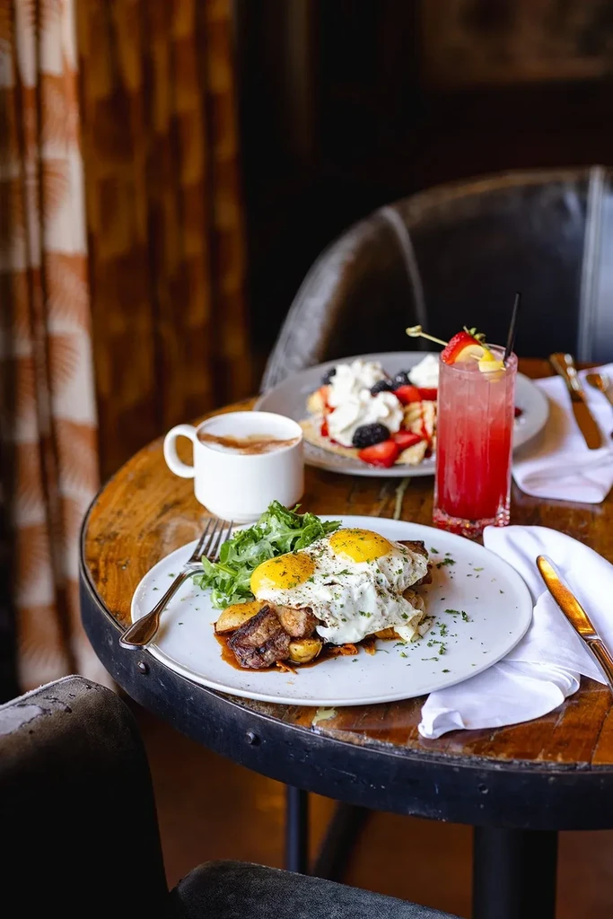 Rustic wooden table with savory eggs, sweet waffles, coffee, and a pink cocktail.
