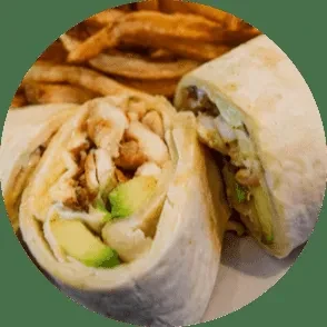 A chicken and avocado wrap, cut in half, with blurred fries.