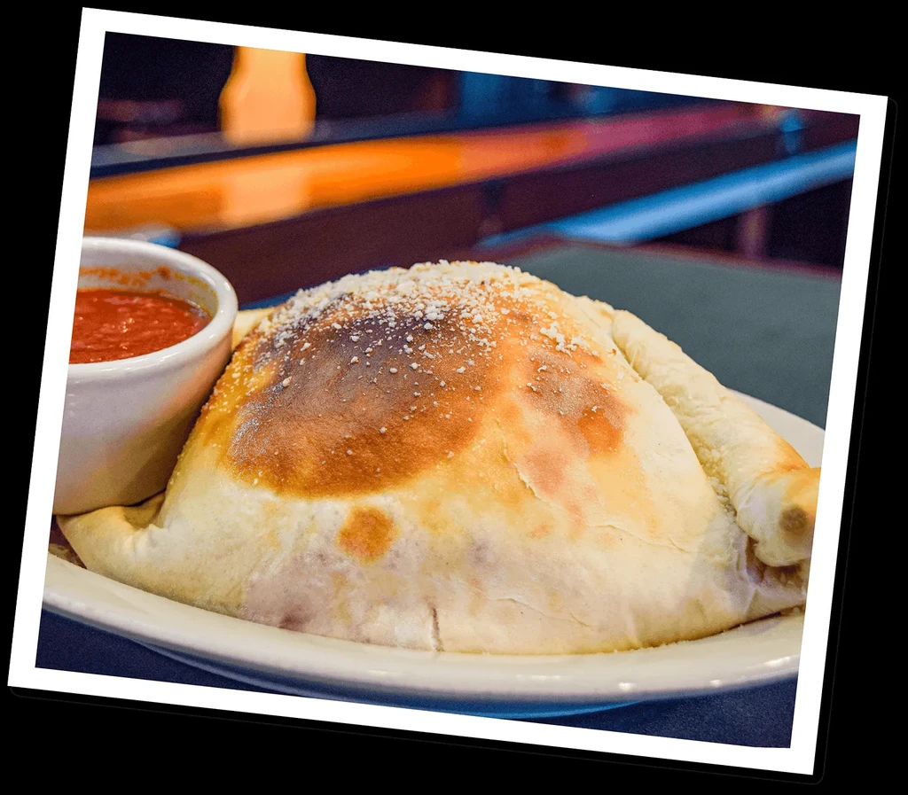 A golden-brown calzone on a white plate with red dipping sauce.