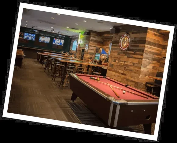 Dimly lit bar interior with red pool table and long counter.