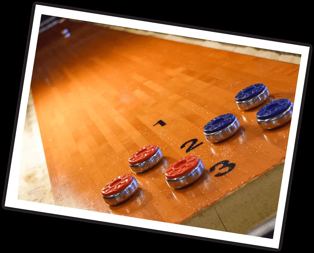 Angled wooden shuffleboard table with red and blue pucks.