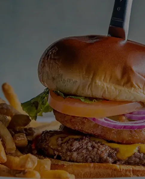 Hamburger skewered with a knife, with cheese, vegetables, and french fries.