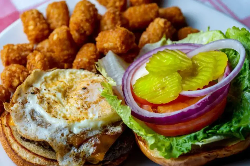 Split burger with egg, cheese, vegetables, pickles, and tater tots.