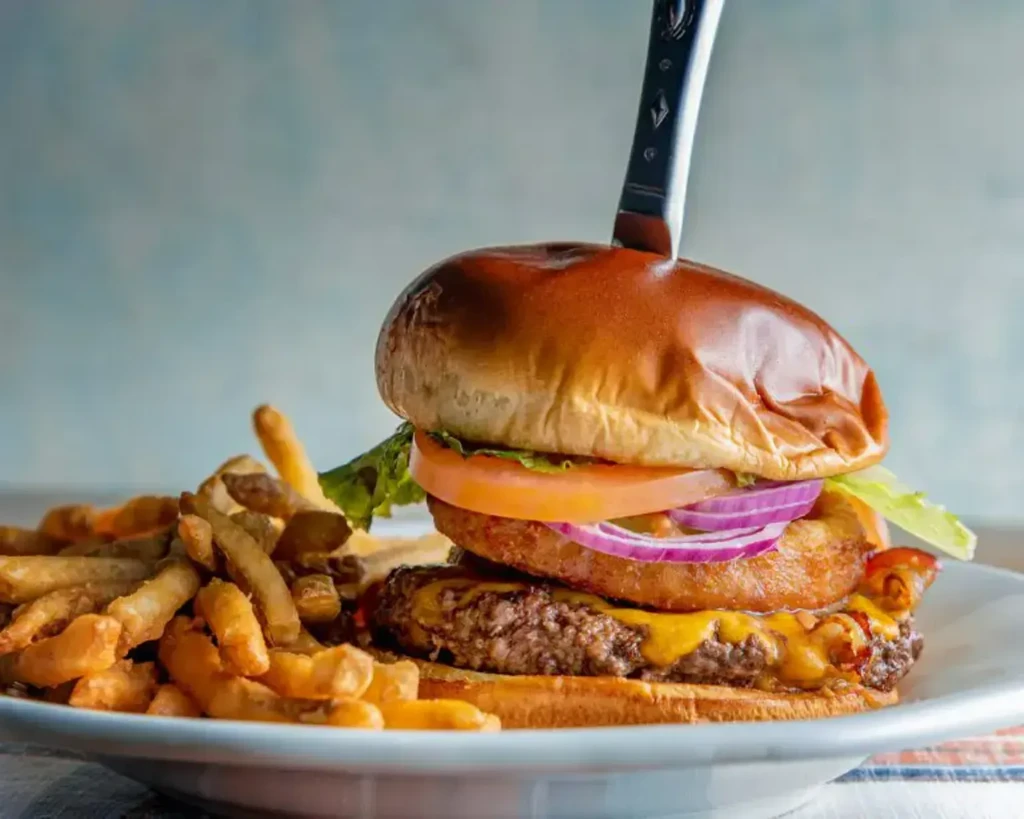 Close-up gourmet burger with melted cheese, fries, and knife.