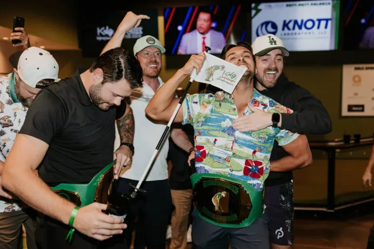 Group of men celebrate golf victory with championship belt and flag.