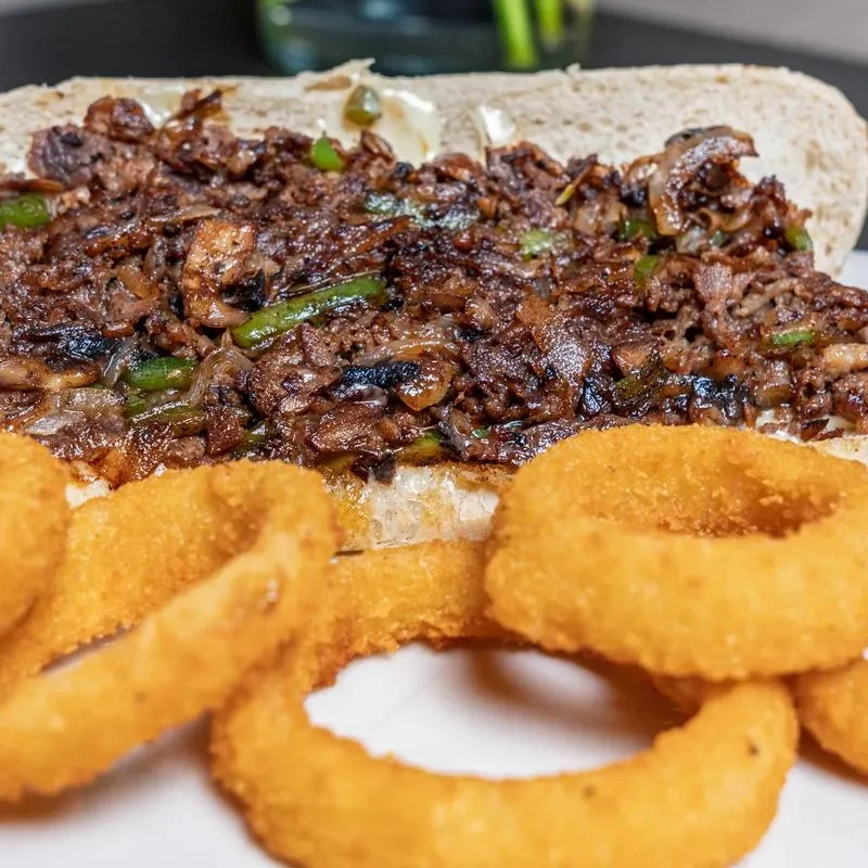 Hoagie sandwich with meat, onions, bell peppers, cheese, and onion rings.