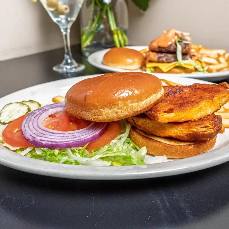 Deconstructed sandwich, cheeseburger, fries, and martini on a dark table.