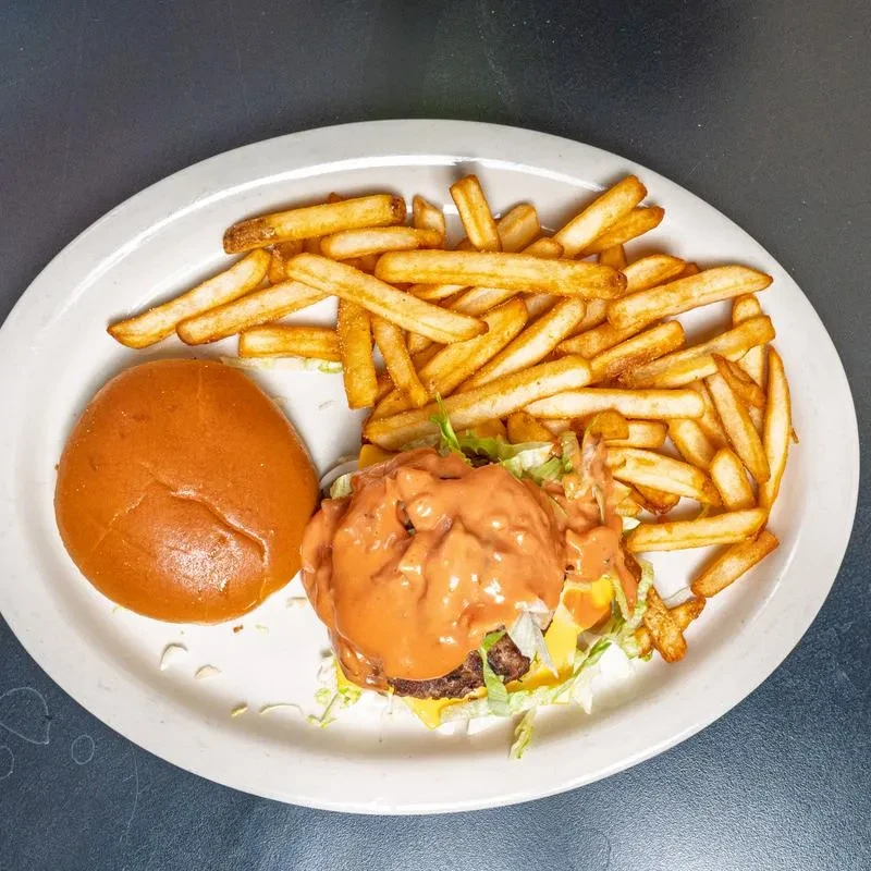 Overhead: burger with separated bun, reddish sauce, and golden french fries.