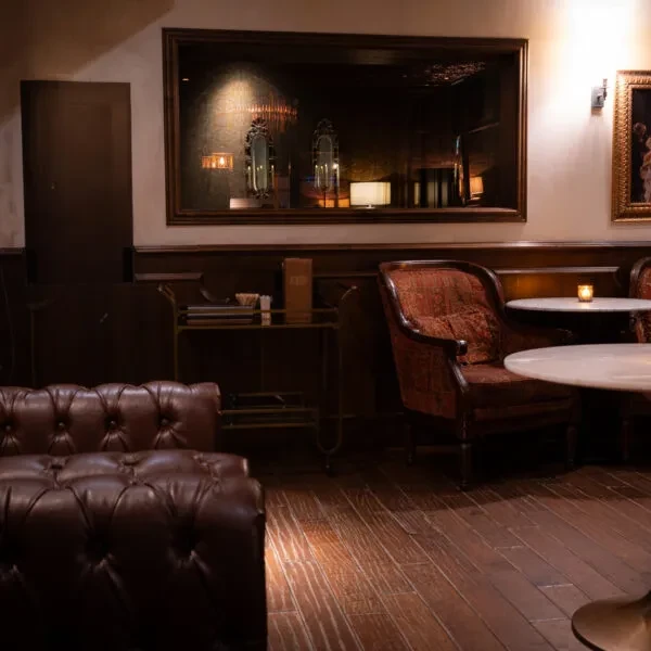 Dimly lit, upscale lounge with dark wood, leather sofa, and candlelit table.