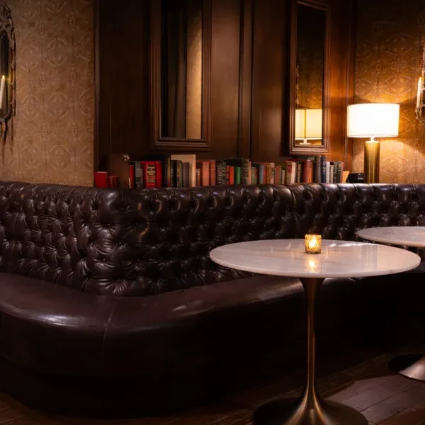Dimly lit interior with dark leather booth, books, and marble tables.