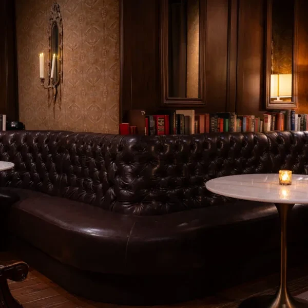 Dark brown tufted leather banquette, marble tables, lit candles, wood paneling.