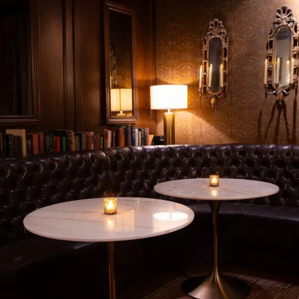 Dimly lit lounge with marble tables, tufted booth, and warm lighting.