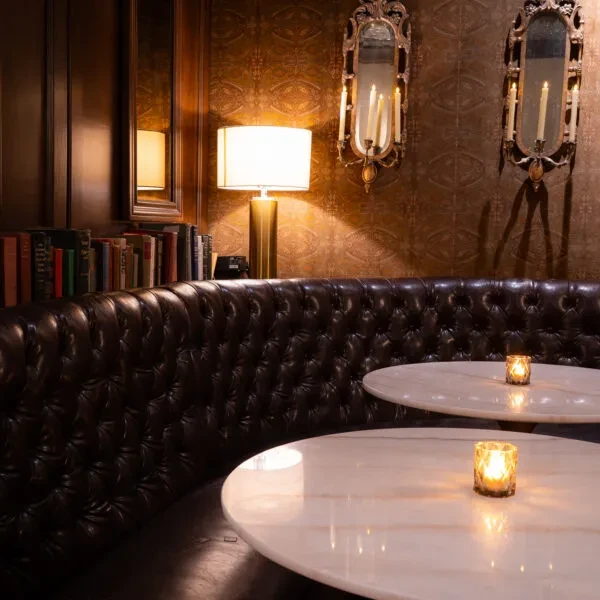 Elegant lounge with a tufted banquette, marble tables, and dim candlelight.