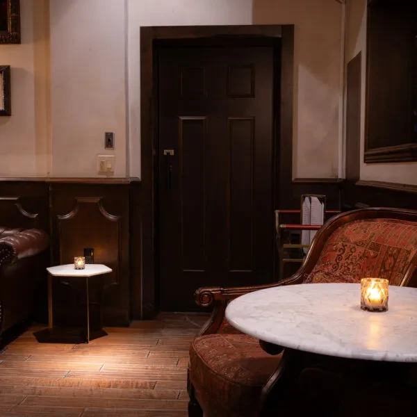 Dimly lit lounge with leather sofa, antique chair, lit candles.