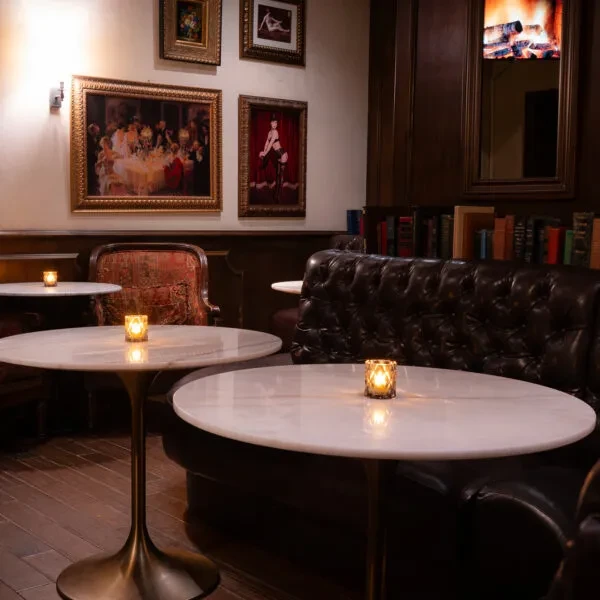Sophisticated lounge with marble tables, tufted booth, framed art, warm light.
