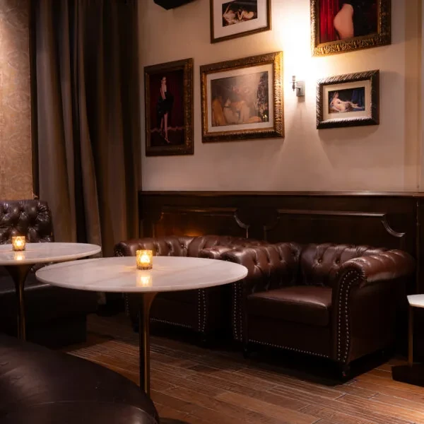 Dark bar interior with marble tables, leather seating, and classical art.