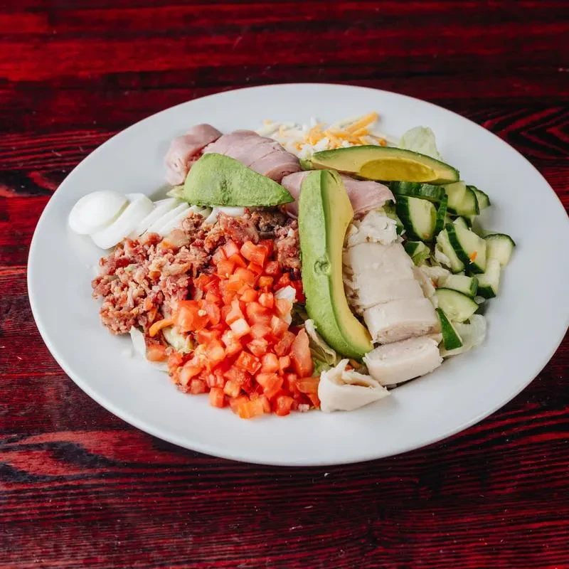 Chef's salad with chicken, ham, egg, avocado on a white plate.