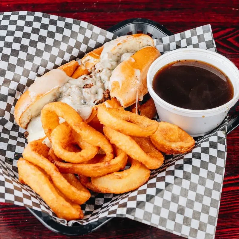 Top-down view of a cheesesteak, fries, and dipping sauce in a basket.