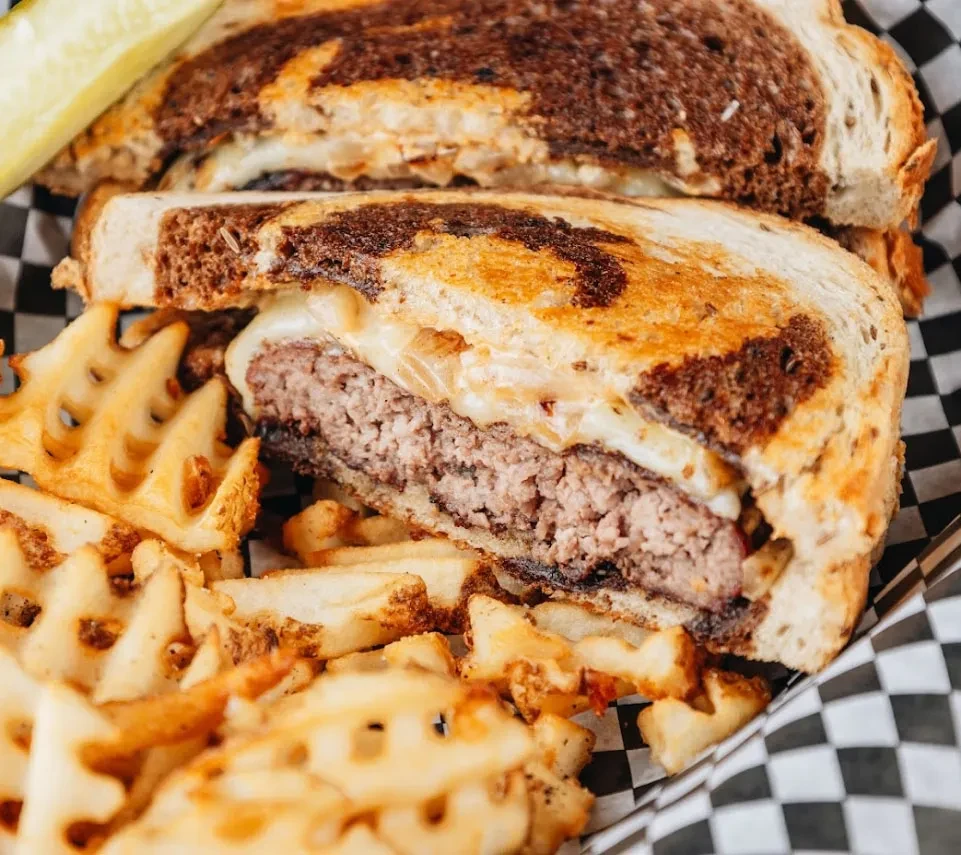 Cut patty melt sandwich, waffle fries, and pickle spear in basket.