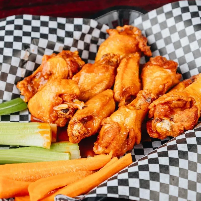 Sauced buffalo chicken wings, celery, and carrots in a basket.