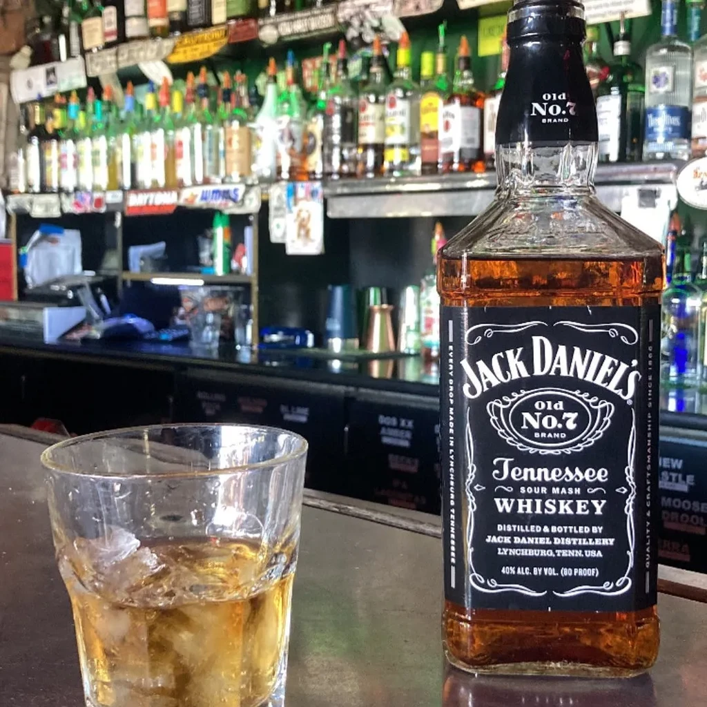 Jack Daniel's bottle and glass of whiskey with ice on bar.