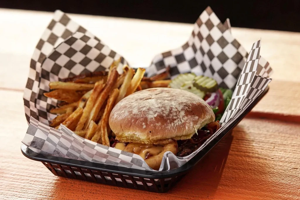 Rustic burger with onion ring and crispy fries in checkered basket.