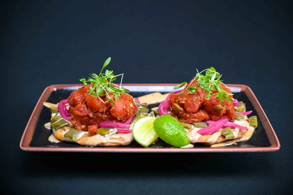 Two appetizers with red tuna tartare, pickled onions, and lime.