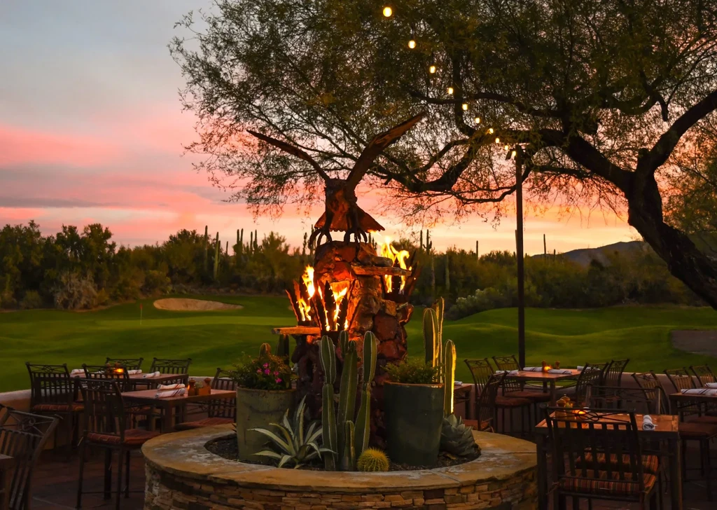 Ornate stone fire pit with eagle sculpture surrounded by desert plants at sunset.
