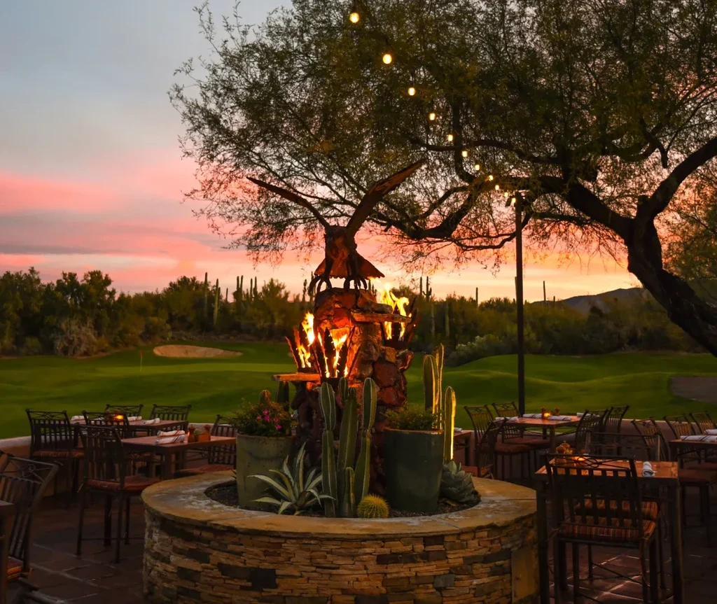 Restaurant patio with fire pit, string lights, and desert sunset.