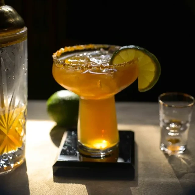 Mushroom-shaped glass holds an amber cocktail with lime and rim.