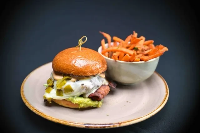 Gourmet burger with bacon, cheese, guacamole, and sweet potato fries.