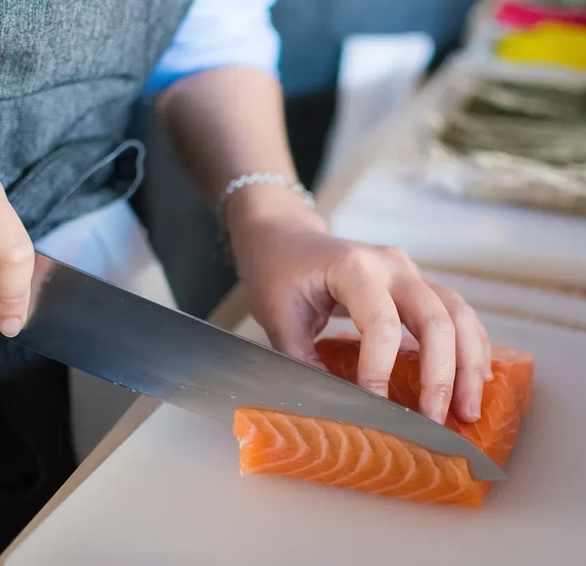 Hands slicing vibrant raw salmon with a knife on a board.