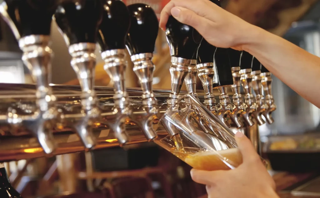 Hands pouring golden beer from a bar tap into a glass.