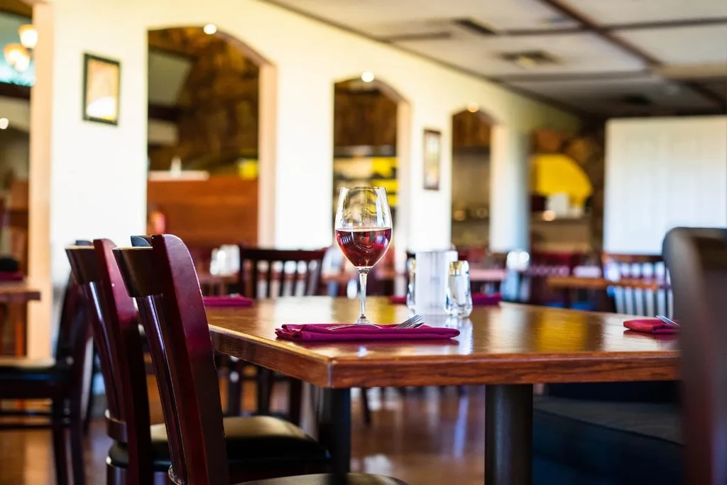 Empty dark wooden restaurant table with red wine and cutlery.